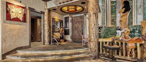 A rustic interior with wooden stairs, a large wooden tree trunk, and a mounted bear.