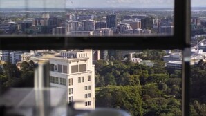 A view from a high-rise window overlooking a cityscape with various buildings, including a prominent white building with multiple windows. - 2BR Apt in the Heart of the City w/ Stunning View (Brisbane City)