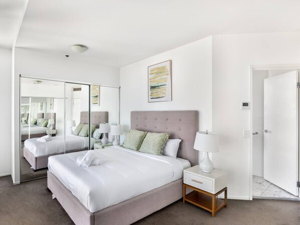 A modern hotel room with a large bed, two bedside tables, a mirror, and a door leading to the bathroom.