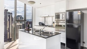 A modern kitchen with a large island, stainless steel appliances, and a view of the city. - 2BR Apt in the Heart of the City w/ Stunning View (Brisbane City)