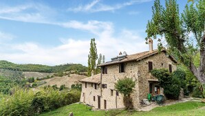 A stone house with a tiled roof, surrounded by greenery and hills.