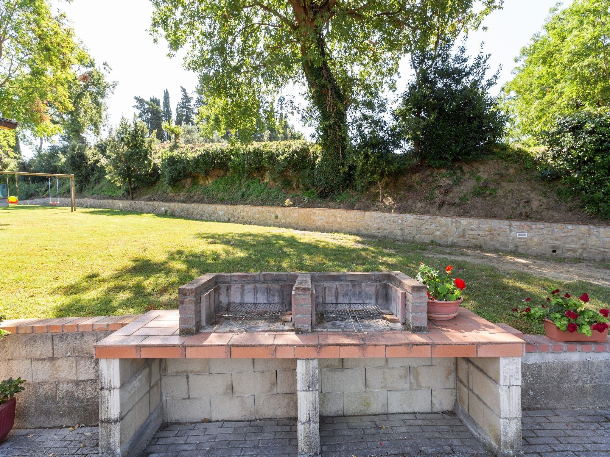 Un barbecue avec une base en pierre, entouré d’une zone herbeuse et d’un mur de pierres.