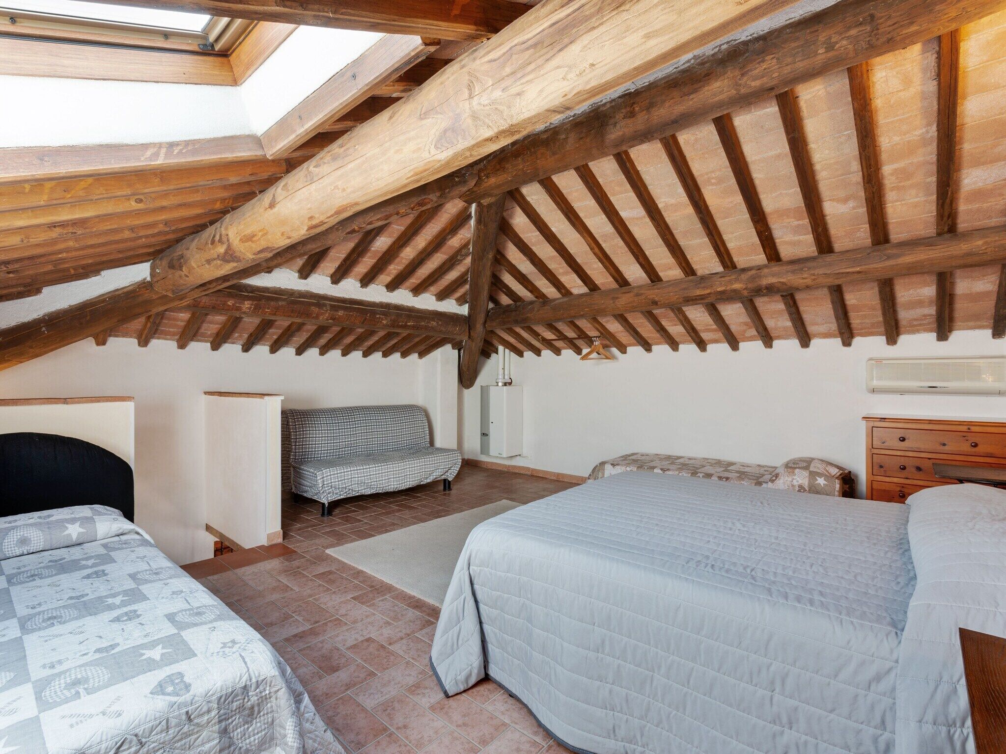 A bedroom with a sloped ceiling, wooden beams, a bed, a sofa, and a dresser.