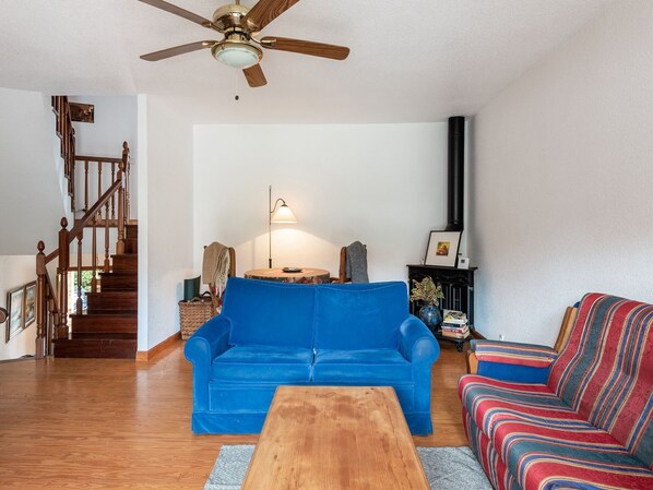 Una sala de estar con un sofá azul, una mesa de centro de madera, un sillón a rayas, una chimenea y una escalera.