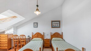 Ein Schlafzimmer mit zwei Holzbett, einem Schreibtisch, einem Stuhl, einer Kommode und einem Dachfenster.