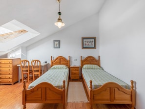 Een slaapkamer met twee houten bedden, een bureau, een stoel, een dressoir en een dakraam.