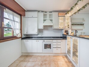 A compact kitchen with white cabinetry, a built-in oven, and a window with curtains.