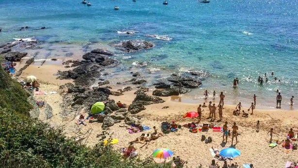 A beach with clear water, rocky areas, and several boats.