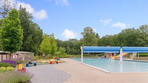 A swimming pool area with a covered deck, a slide, and a small building in the background. - chalet in the woods with pool (Vledder)