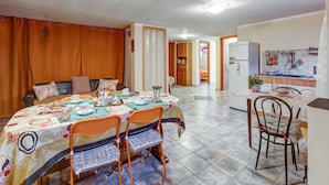 A dining area with a table set for four, surrounded by chairs, and a kitchen area with a refrigerator and utensils visible.