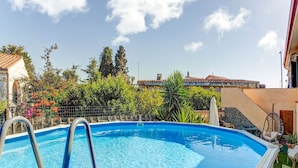 A swimming pool with a metal ladder, surrounded by greenery and buildings.