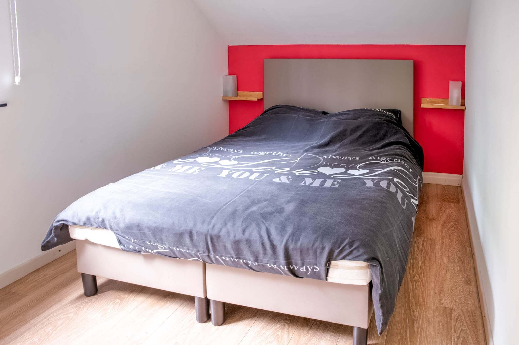 Una camera da letto con un letto, una parete decorata in rosso e un pavimento in legno.