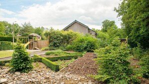 Ein Garten mit einer hölzernen Spielanlage, einem Schuppen und einem großen Gebäude im Hintergrund.