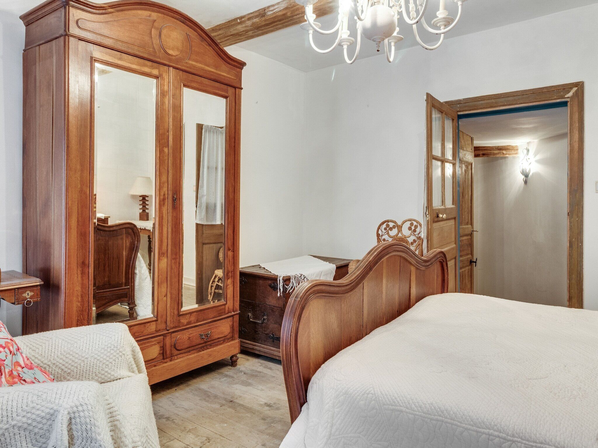 Een slaapkamer met een houten garderobe, een bed en een spiegel.
