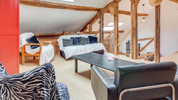 A cozy loft bedroom with a sloped ceiling, wooden beams, a bed with patterned pillows, a dining table, and a red cabinet. - Charming Stay in Viroinval (Viroinval)