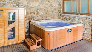 Un sauna en bois avec un mur de pierres en arrière-plan, un meuble en bois doté d’une porte en verre et une fenêtre avec des panneaux de verre dépoli.