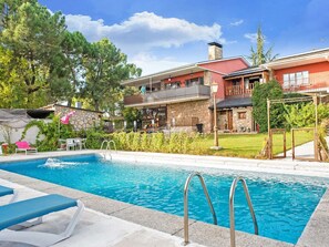 A swimming pool with lounge chairs, a stone building with a balcony, and a grassy area with trees. - Tranquil Garden Hideaway (Galapagar)