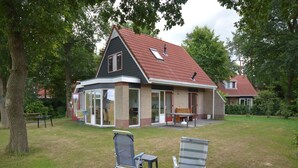 A house with a sloped roof, large windows, and a patio area with two lawn chairs.