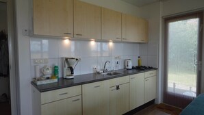 A compact kitchen with light wooden cabinets, a black countertop, and basic appliances.