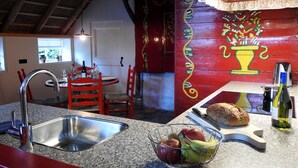 A kitchen with a granite countertop, stainless steel sink, and a dining area with red chairs and a table.