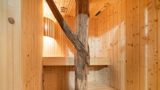 Interior d'una cabana de fusta amb una biga de fusta al centre, una banca i un sostre inclinat.