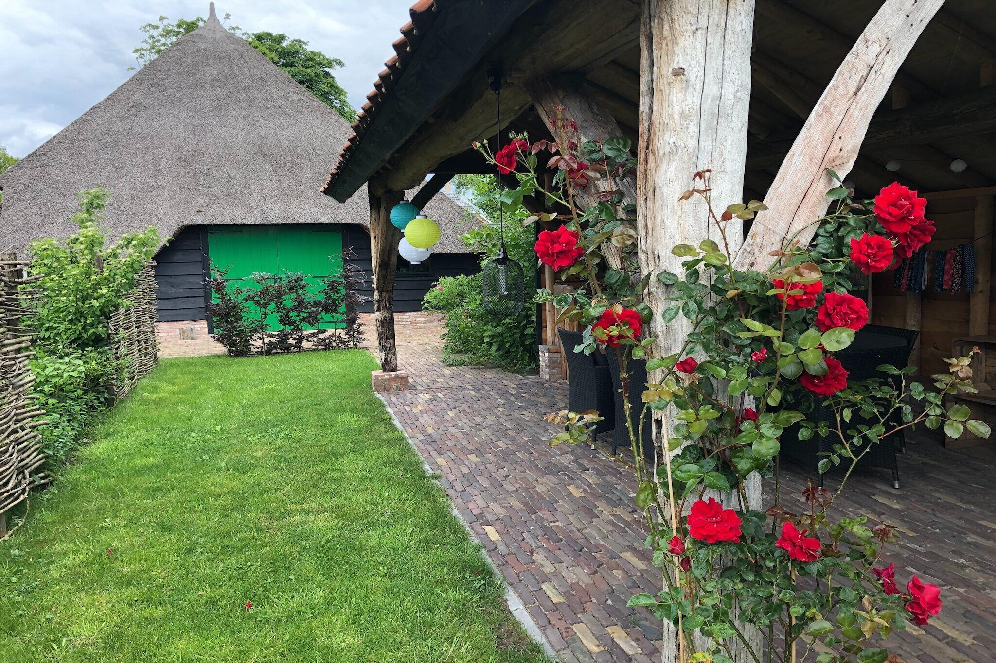 Ein rustikales Gebäude mit einem Strohdach, einem Ziegelweg und einem Rosengarten mit roten Rosen.