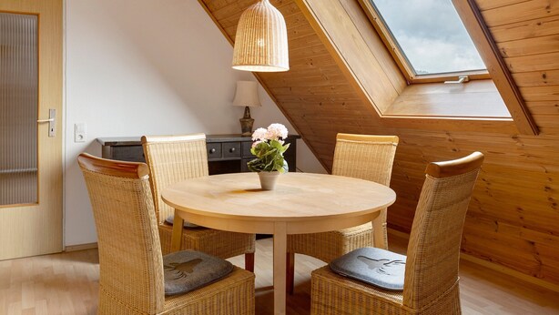 A dining area with a round table, wicker chairs, a hanging light fixture, and a skylight. - Apartment 'Haus Am Südhang' with Shared Garden, Balcony and Wi-Fi (Lenzkirch)