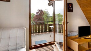 A room with a sliding glass door leading to a balcony, a white sofa, a small table, and a TV on a wooden stand. - Apartment 'Haus Am Südhang' with Shared Garden, Balcony and Wi-Fi (Lenzkirch)