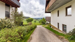 A narrow gravel path flanked by buildings with balconies, leading to a rural landscape. - Apartment 'Haus Am Südhang' with Shared Garden, Balcony and Wi-Fi (Lenzkirch)