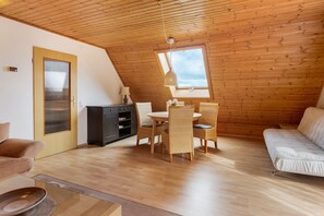 A room with a wooden ceiling, a dining table with chairs, a sofa, and a small cabinet.