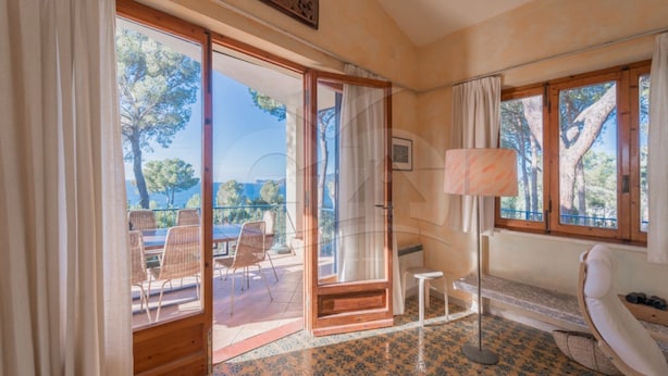 A room with a large sliding glass door leading to an outdoor area with a table and chairs. There is a lamp, a bench, and a small stool inside the room. - VILLA MADONNA DELLE GRAZIE (Capoliveri)