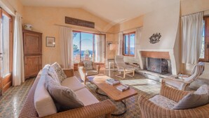 A cozy living room with a fireplace, comfortable seating, and large windows offering a view of the outdoors. - VILLA MADONNA DELLE GRAZIE (Capoliveri)