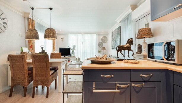 A modern kitchen with dark cabinets, a microwave, and a dining area with wicker chairs and a wooden table. - Holiday Home in Garderen by Veluwe (Garderen)