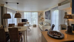 A modern living room with a dining area, featuring wicker furniture, a flat-screen TV, and a fireplace. - Holiday Home in Garderen by Veluwe (Garderen)