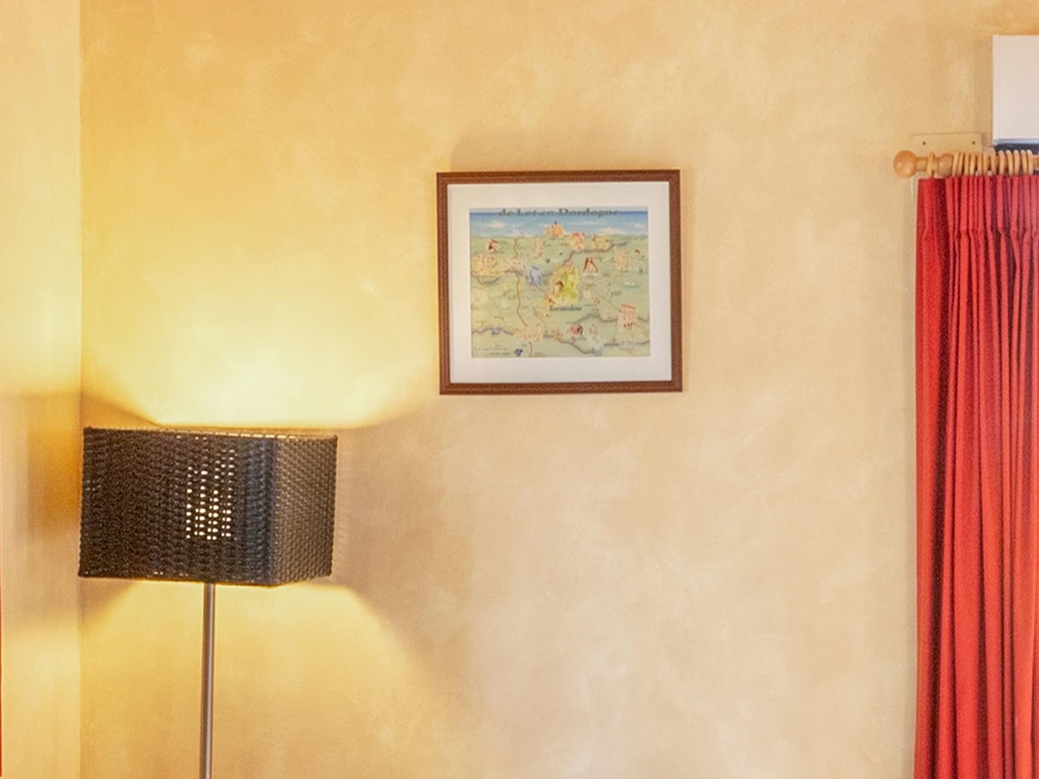 Una stanza con una mappa incorniciata appesa al muro, una lampada e una tenda rossa.