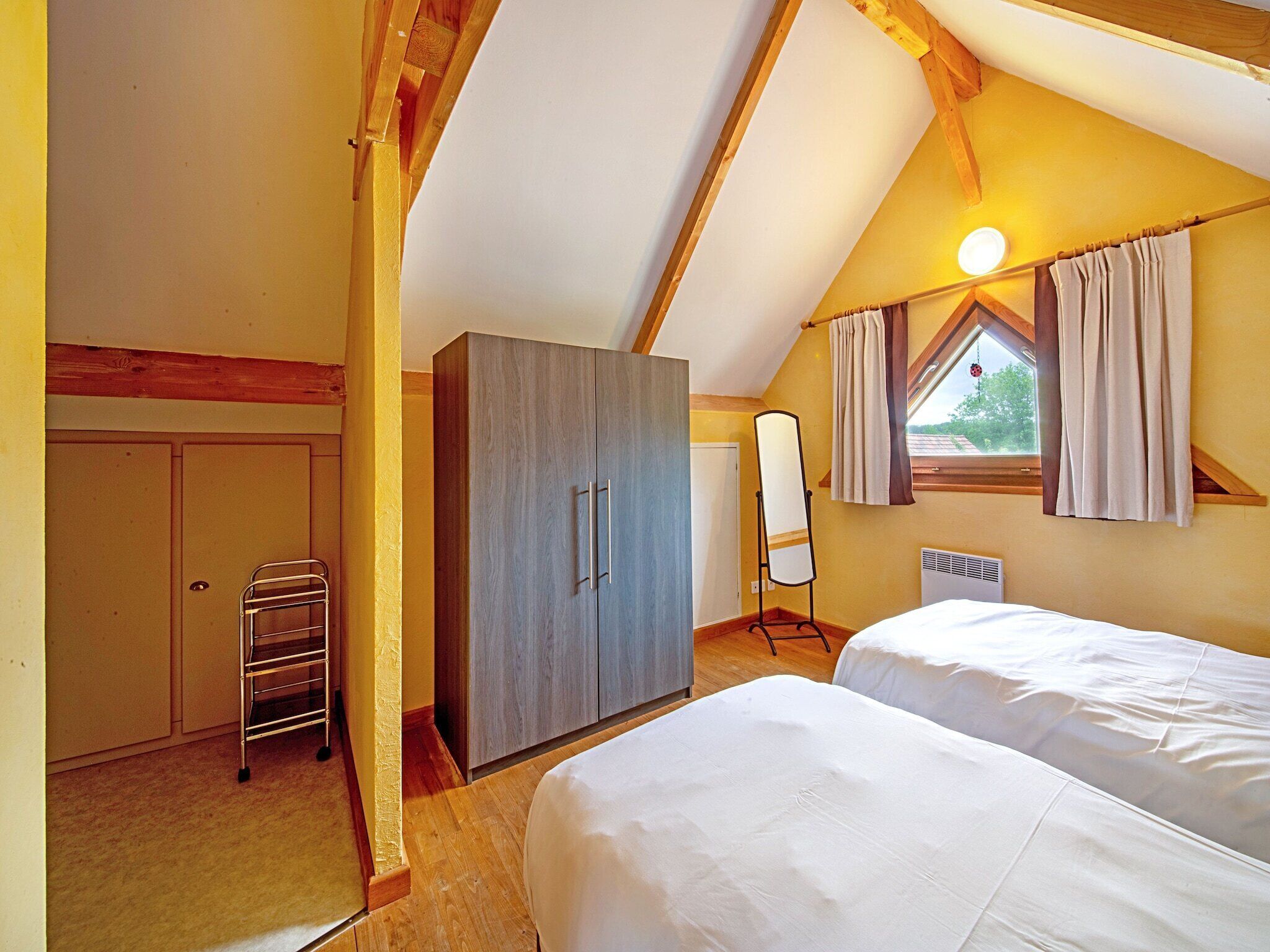 Ein Schlafzimmer mit zwei Betten, einem Kleiderschrank, einem Heizkörper und einem Fenster mit Vorhängen.