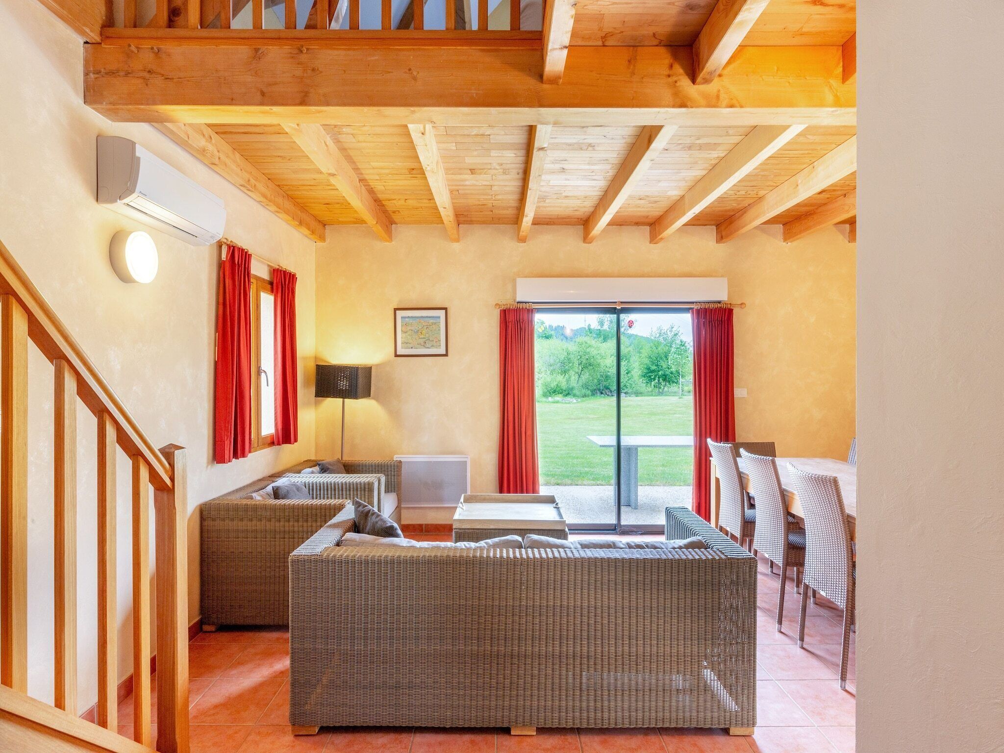 A cozy room with a wooden ceiling, a sofa, a table, and a view of a garden through a glass door.