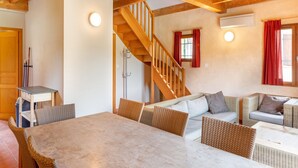 Un espacio de sala acogedor con una escalera de madera, muebles de mimbre y una mesa de comedor.
