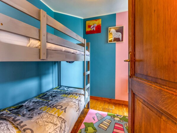A bunk bed room with a wooden ladder, a colorful rug, and a door with a wooden frame.