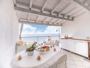 Een eethoek met een tafel voor twee personen, een wit kastje en uitzicht op de zee.