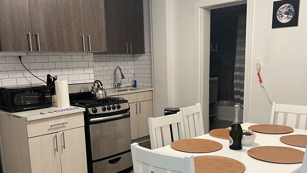 A modern kitchen with white cabinets, a stove, and a dining table with chairs.