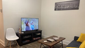 A living room with a flat-screen TV, a sofa, a coffee table, and a bookshelf.