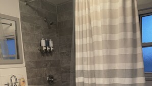 A bathroom with a bathtub, a shower, a vanity with a mirror, and a window.