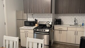A kitchen with a stove, microwave, and coffee maker. There is a white chair and a table with a placemat.