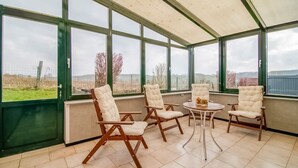 A conservatory with four cushioned chairs and a small table, large windows offering a view of the countryside. - Cottage in Vaux-sur-Sûre with garden (Vaux-sur-Sûre)