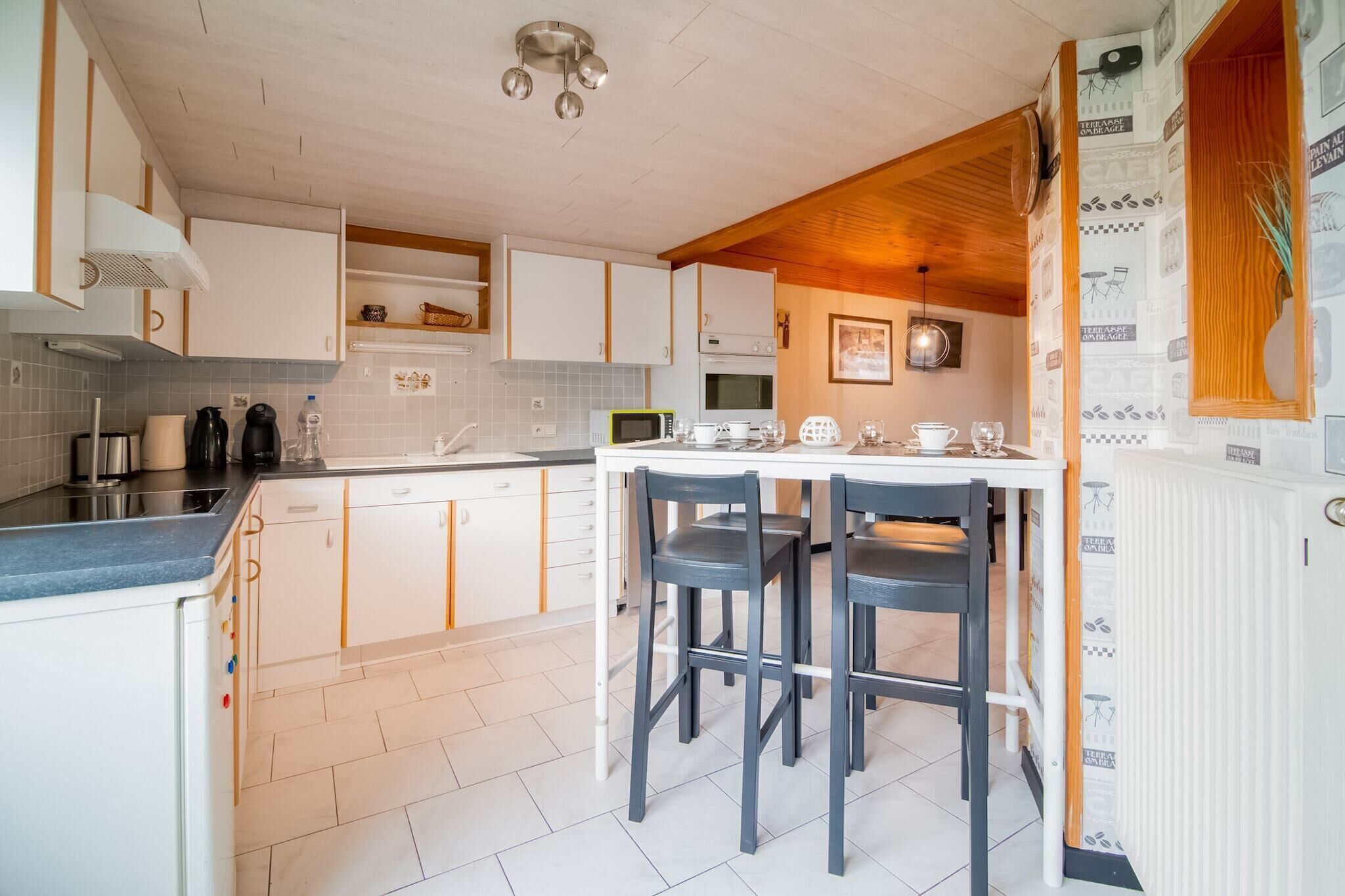Une cuisine moderne avec des meubles blancs, un îlot central doté de tabourets, un four à micro-ondes et un évier.