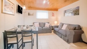 A cozy living room with a dining area, wooden ceiling, grey sofas, and a TV on the wall. - Cottage in Vaux-sur-Sûre with garden (Vaux-sur-Sûre)