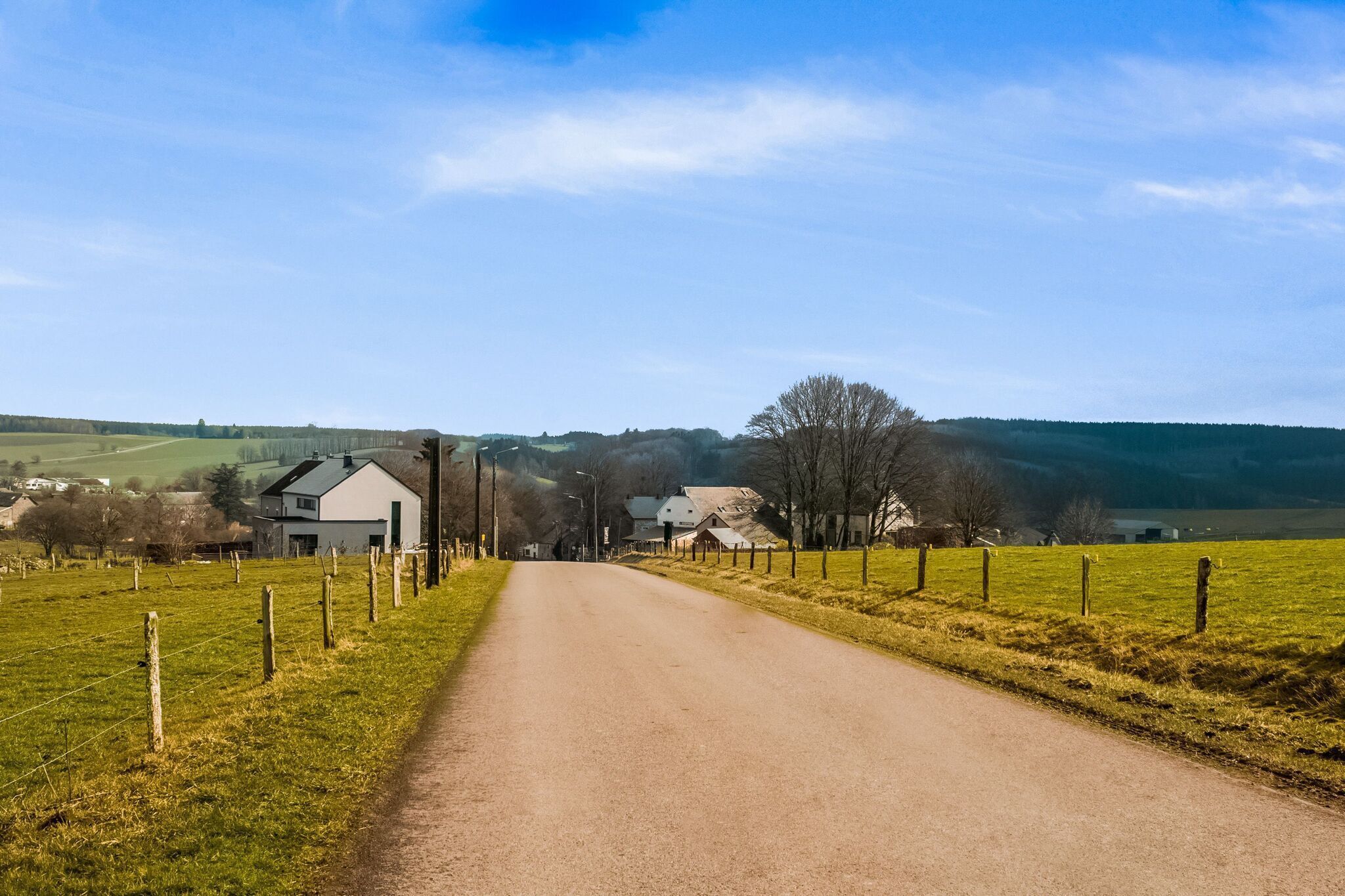 A rural road flanked by green fields and houses.