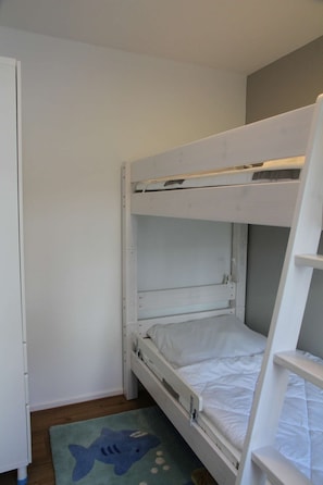 Kerrossängyllä varustettu huone, jossa on tikkaat, pieni matto, jonka kuvio esittää hai, ja valkoinen vaatekaappi.