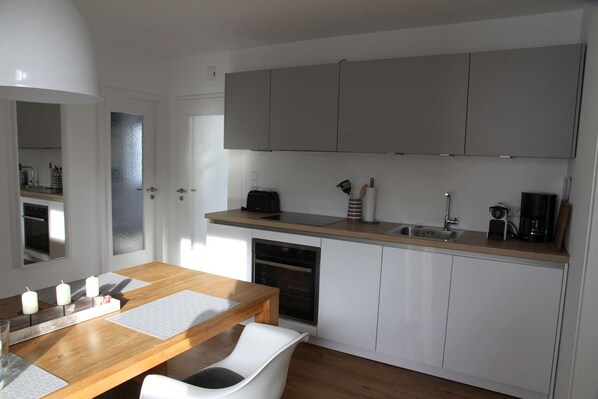 A modern kitchen with white cabinets, a wooden countertop, and a dining area with a table and chairs.